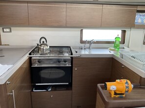 A compact kitchenette with a stove, oven, sink, and a small window. - Sun-Kissed Sailing Adventure in the Ionian Islands, Lefkada (Lefkada)