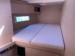 Una cama compacta con un compartimento de almacenamiento integrado debajo, una ventana pequeña para luz natural y un panel de control en el lado izquierdo.