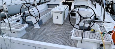 Cubierta de barco con timón, panel de control y zona de estar.