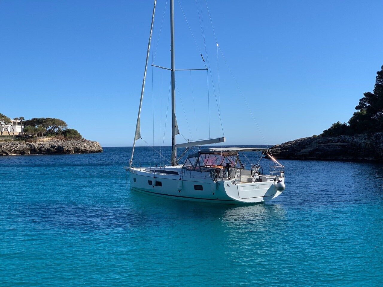 Ein Segelboot liegt vor einer felsigen Küste in klarem, blauem Wasser.