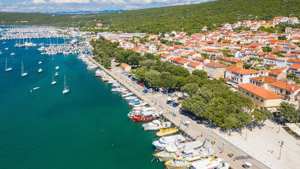 A coastal town with a marina, residential buildings, and a hilly backdrop. - Sun-Kissed Sailing Adventure in Northern Croatia (Punat)