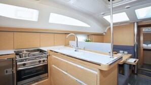 Una pequeña cocina compacta con fregadero, estufa y horno; una zona de estar con mesa y sillas; y una ventana que proporciona luz natural.