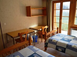 Une chambre avec deux lits, un bureau et une chaise. Il y a une fenêtre donnant sur l’extérieur.