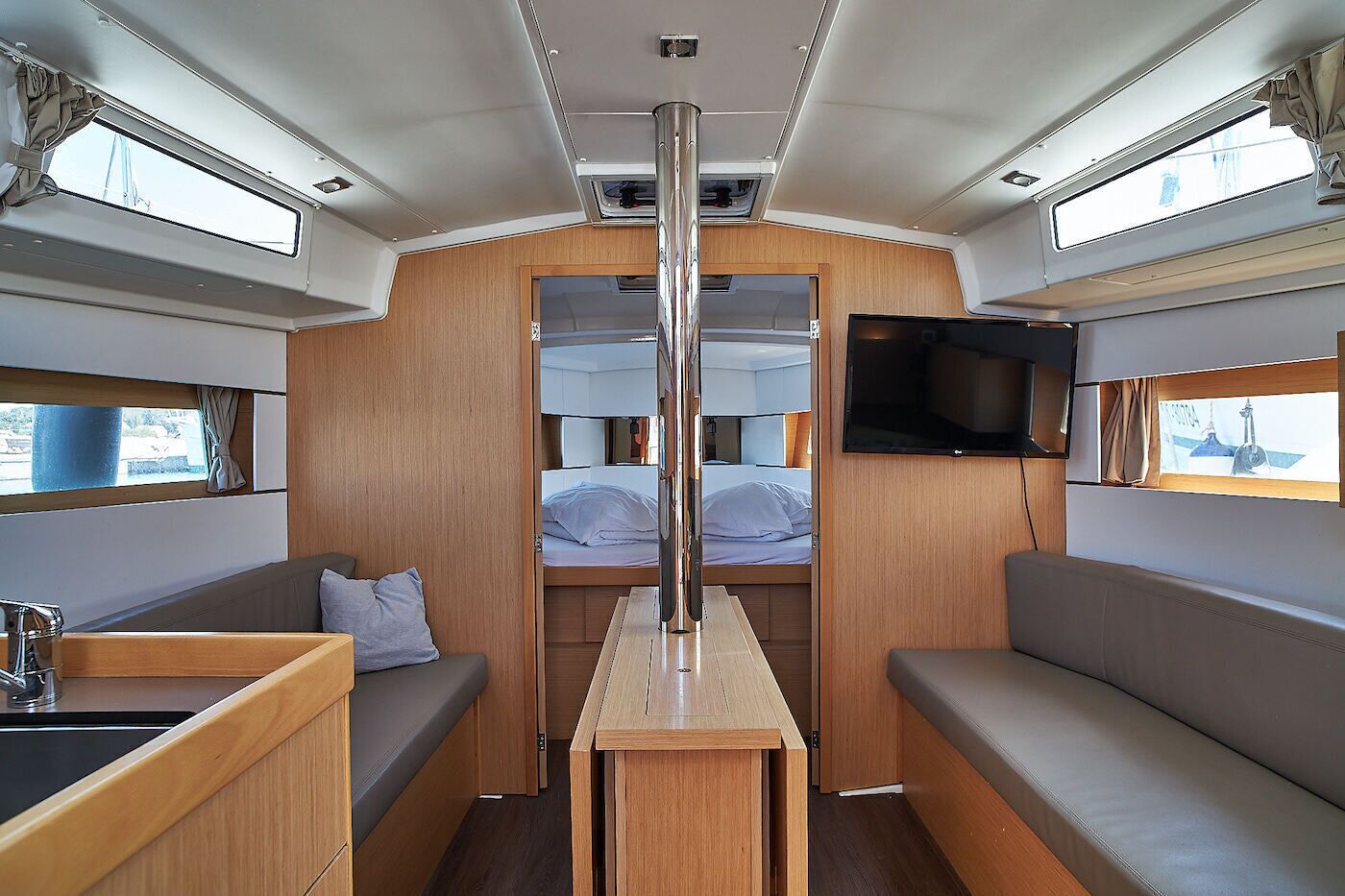 A compact interior with a central table, two seating areas, a TV mounted on the wall, and a window on the left.