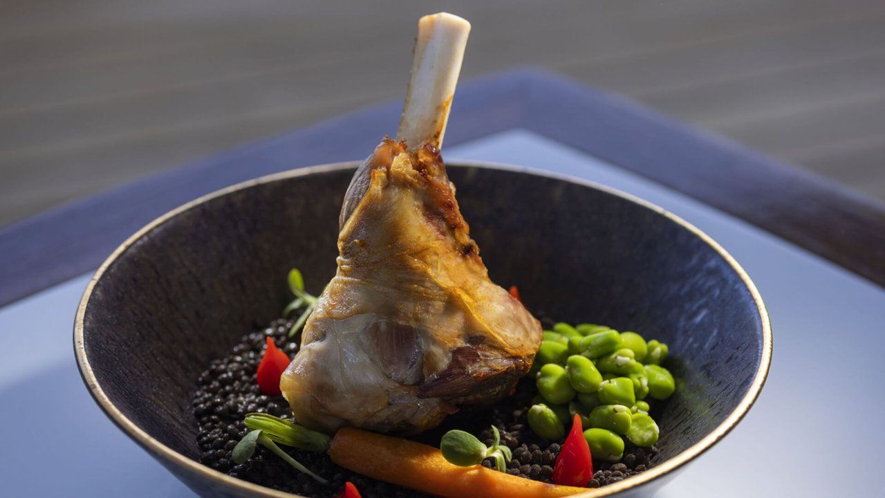 Un plat composé d’une pièce de viande avec un os, de petits pois et de légumes, servi dans une assiette.