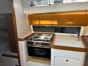 A compact galley with a stove, oven, sink, and wooden cabinetry. - Sun-Kissed Sailing Adventure in Split, Croatia (Split)