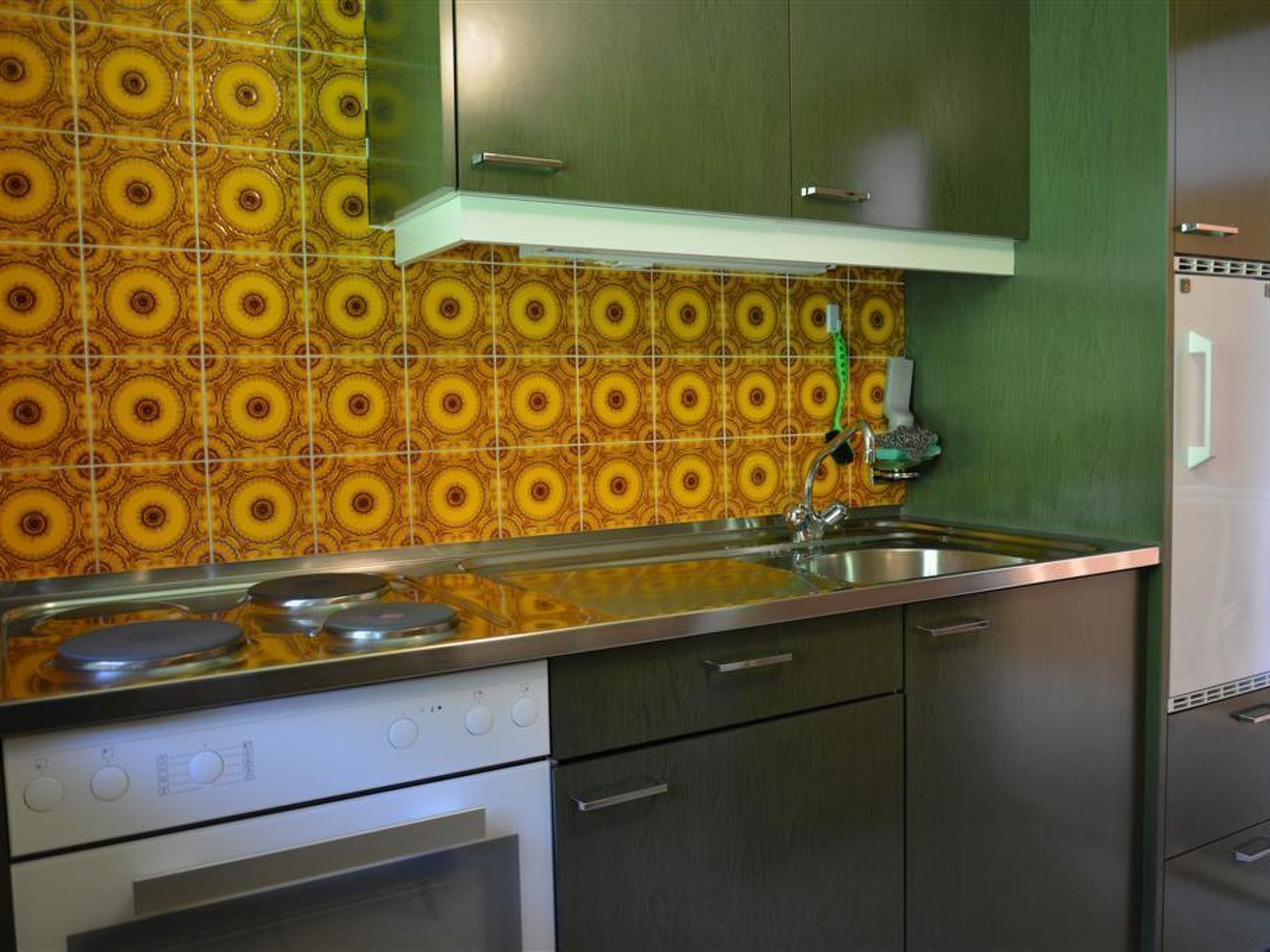 Et køkken med et mønstret backsplash, rustfrie apparater og grønne skabe.