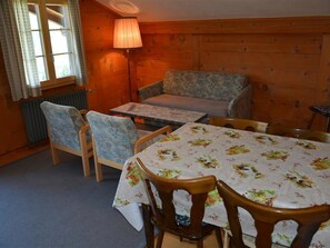 A cozy room with a wooden interior, a sofa, two chairs, a table with a floral tablecloth, and a lamp. - Rehweid (2. Stock) Appartement/Fewo, Dusche oder Bad, WC 5-Bettwohnung by Interhome (Gstaad)
