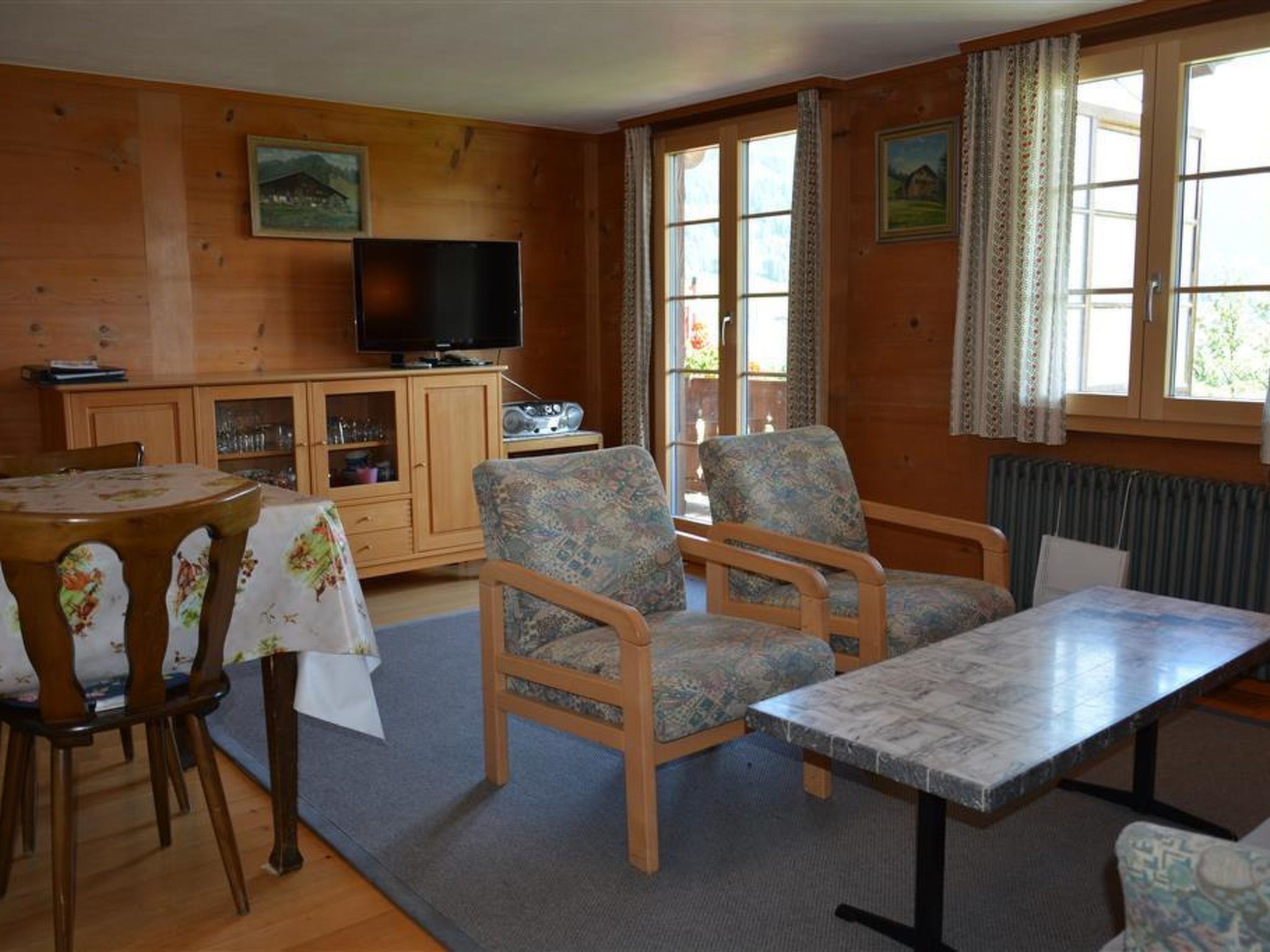 Uma sala de estar aconchegante com paredes de madeira, uma televisão, uma mesa de jantar com cadeiras e uma janela grande com cortinas.