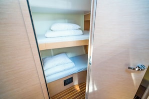 Een compacte, goed verlichte kamer met een stapelbed, een houten deur en een klein plankje met opgevouwen handdoeken.
