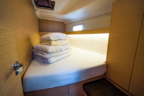 Een klein bed met een stapje opgevouwen handdoeken, een klein raam en een deur met een handgreep.