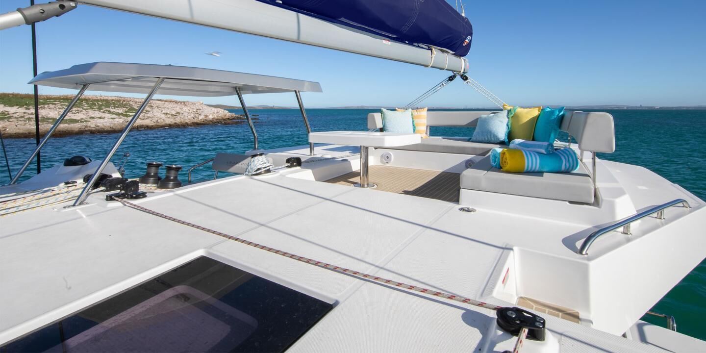 Um convés de barco com área de estar branca, toldo e vista para o mar.