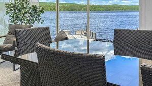A glass table with wicker chairs, a potted plant, and a view of a lake and forest. - Awesome home in Lycksele with house sea view (Lycksele)
