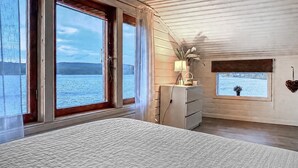 A bedroom with a large bed, a dresser, a lamp, and a view of a lake through two windows. - Awesome home in Lycksele with house sea view (Lycksele)