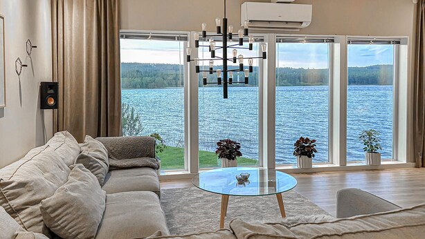 A living room with a sofa, a glass coffee table, and a view of a lake through large windows. - Awesome home in Lycksele with house sea view (Lycksele)