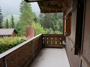 Een houten balkon met uitzicht op een bebost gebied en een huis op de achtergrond.