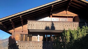 Una cabaña de madera con balcón, ventanas grandes y vistas a las montañas.