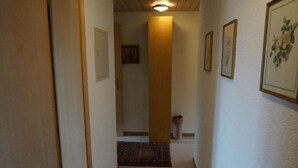 Un pasillo estrecho con una puerta de madera a la izquierda, un cuadro enmarcado a la derecha y una alfombra que conduce a una habitación.