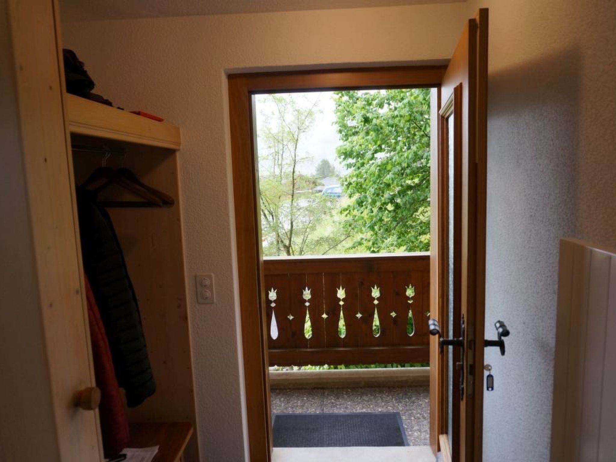 Een open deur die uitkomt op een balkon met houten hekwerk en decoratieve details.