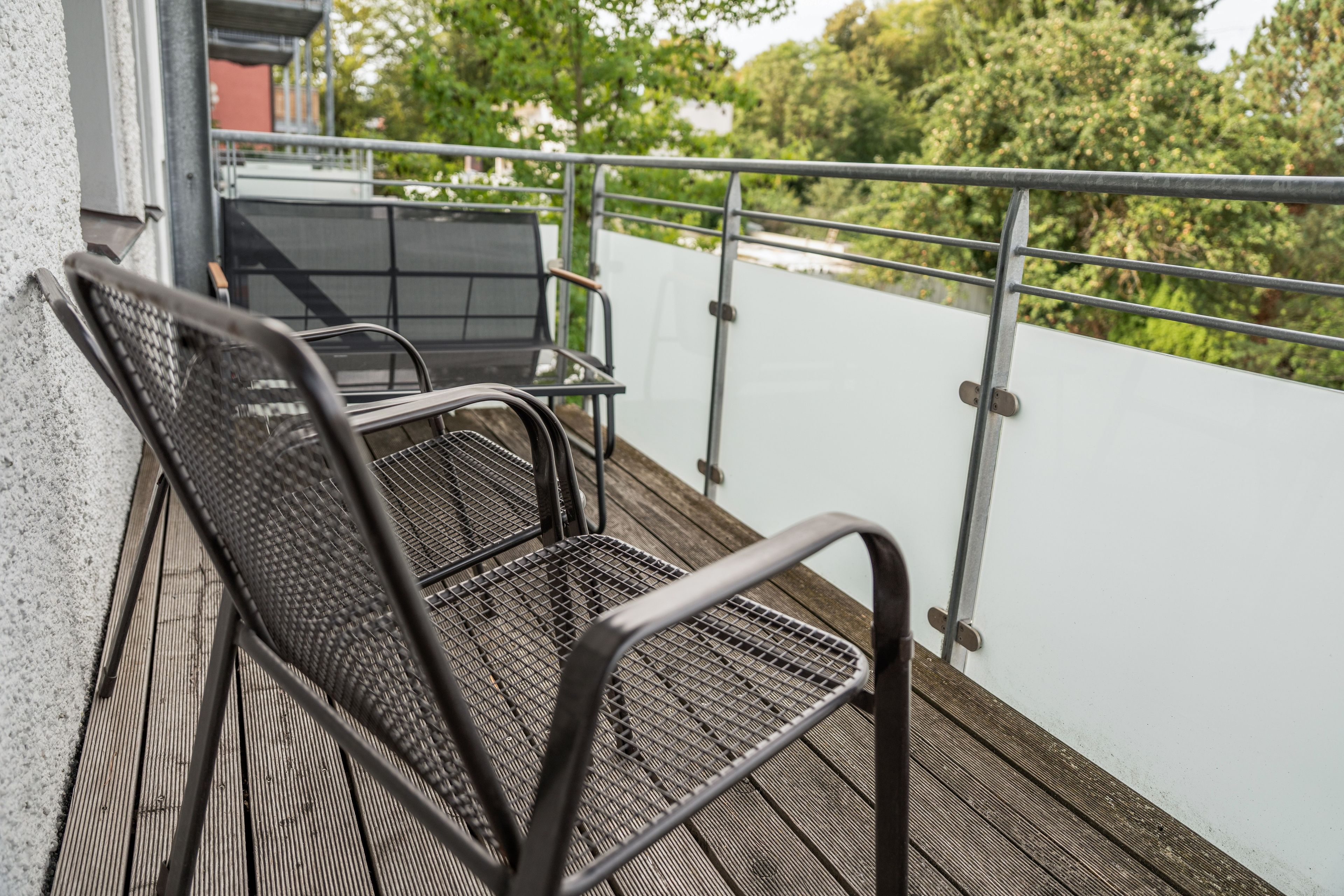 Un balcón con sillas y una mesa de metal, con vistas a un paisaje verde.