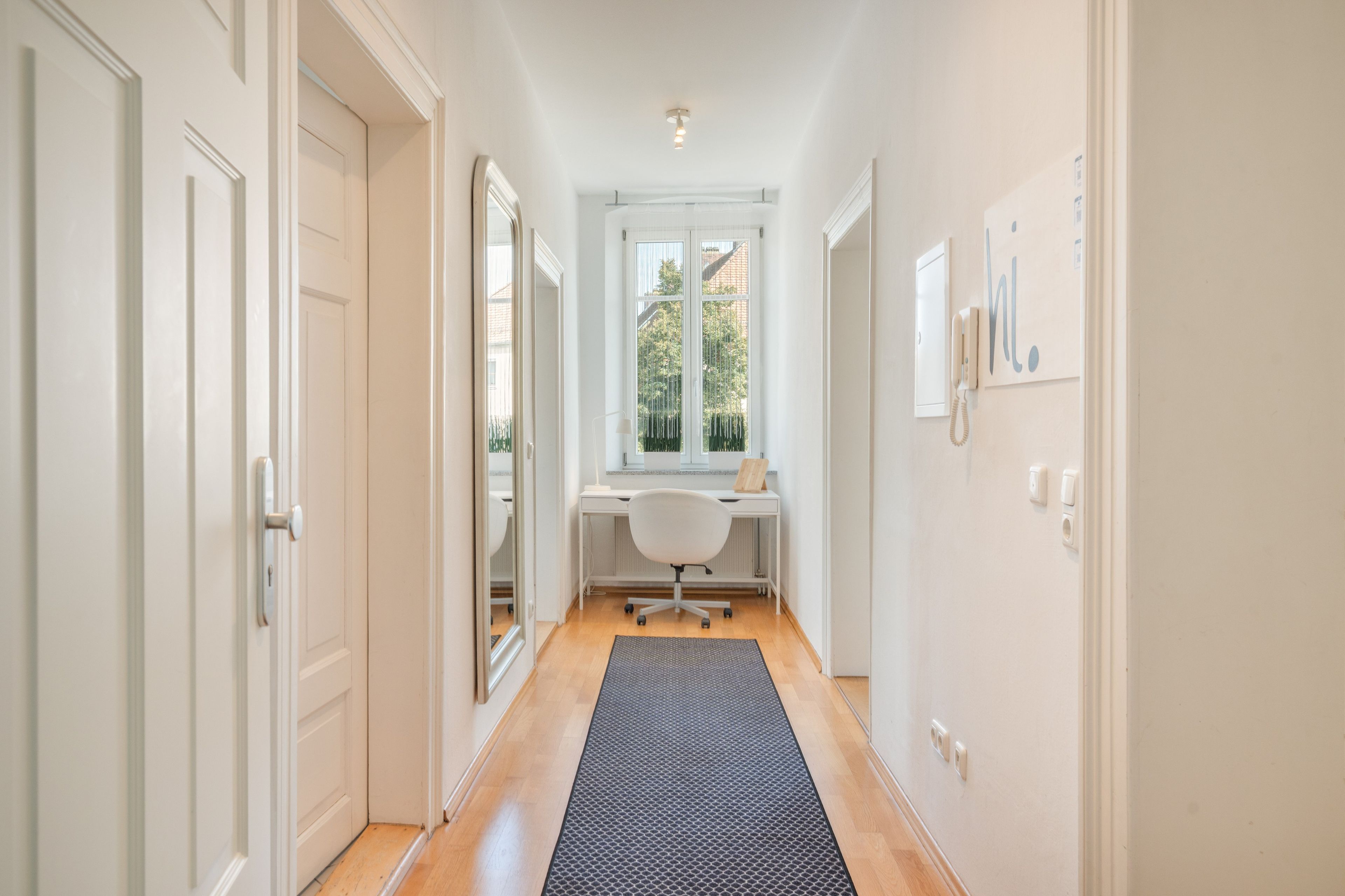 Un couloir avec un bureau, une chaise et une fenêtre donnant sur un paysage verdoyant.