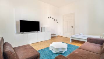 Una sala de estar moderna con un televisor de pantalla plana, muebles blancos, un tapete azul y una puerta con manija.