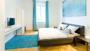 A bedroom with a bed, a TV, a window with curtains, a painting, and a blue rug. - Stadt Land Fluss Apartment 2 (Regensburg)