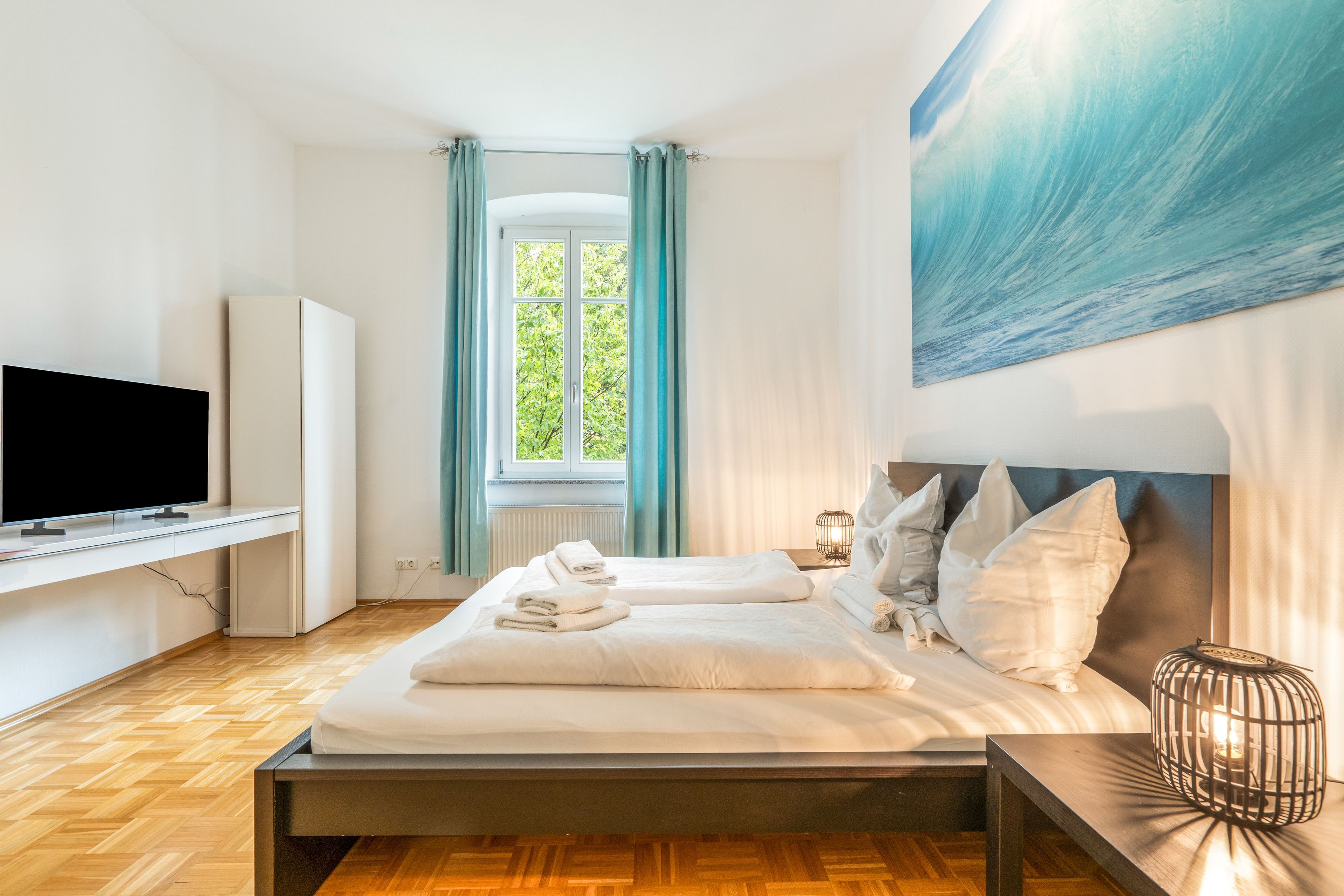 A hotel room with a bed, a television, a window with curtains, and a painting on the wall.