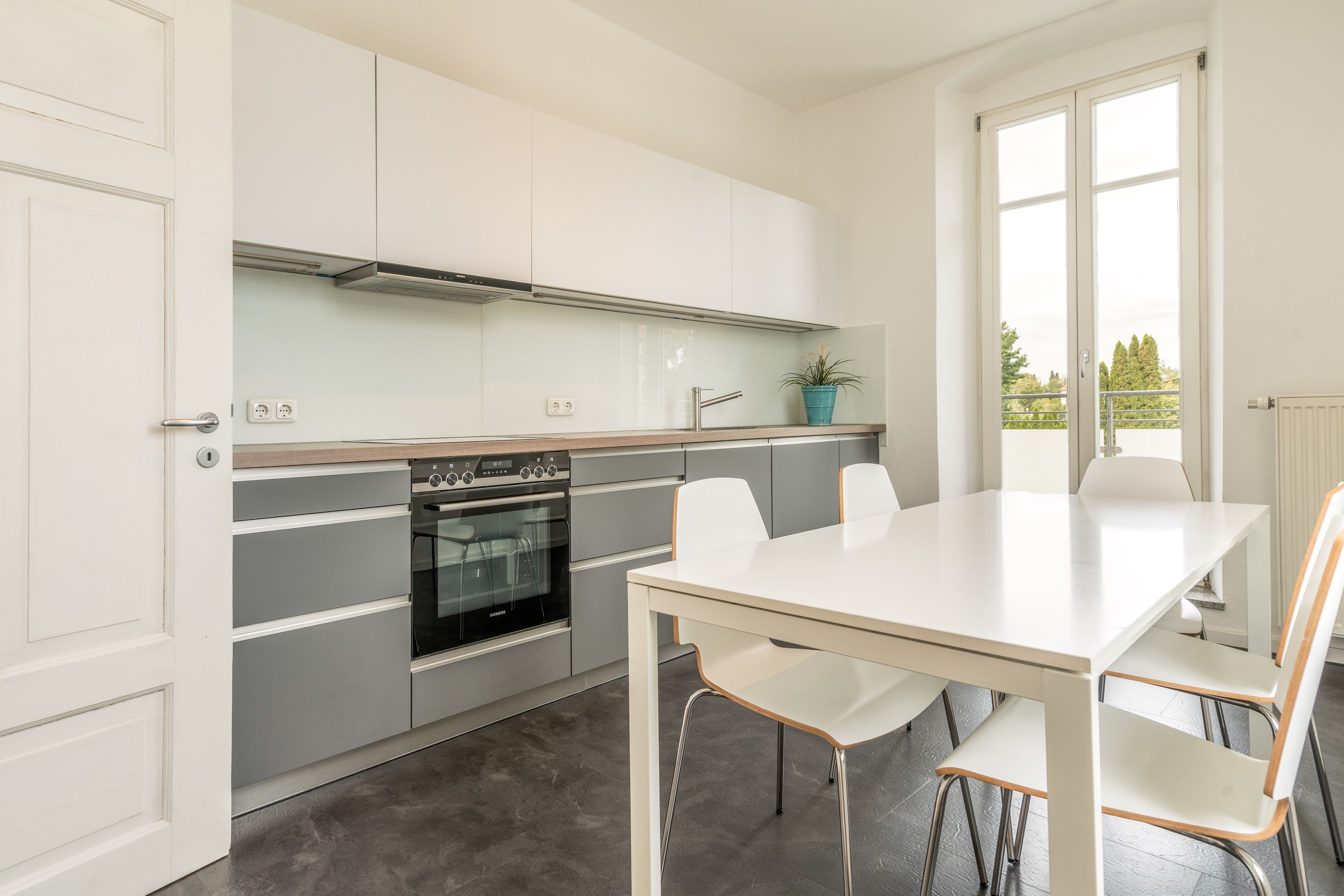 Cocina moderna con horno integrado, una mesa de comedor con sillas y una ventana con vistas a árboles.