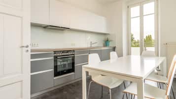 Cocina moderna con horno integrado, una mesa de comedor con sillas y una ventana con vistas a árboles.
