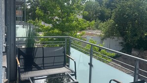 A balcony with a glass barrier, outdoor seating, and a view of trees and a swimming pool. - Stadt Land Fluss Apartment 2 (Regensburg)