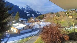 Paisaje de montaña con picos nevados, un edificio de madera y cielo despejado.