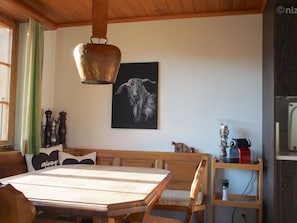 Ein Essbereich mit Holztisch und Bänken, einer hängenden Kupferleuchte und einem Schwarz-Weiß-Gemälde einer Ziege an der Wand.