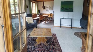 Una sala acogedora con una mesa de centro de madera, un sillón azul y una zona de comedor con una mesa y sillas de madera.