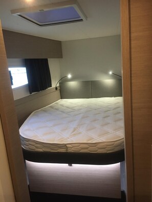Un lit compact doté d’une tête de lit, d’un puits de lumière au-dessus et d’une fenêtre avec des rideaux.