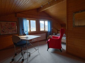 A room with a desk, two chairs, a bed, and a large window with curtains. - Weidli, Chalet Appartement/Fewo, Dusche oder Bad, WC 4-Bettwohnung by Interhome (Zweisimmen)