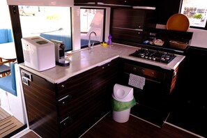 Een kleine keuken met koffiezetapparaat, spoelbak, fornuis en vuilnisbak.