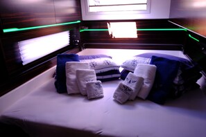 A bed with pillows and folded towels, a window with blinds, and a wooden headboard. - Sun-Kissed Sailing Adventure in Sibenik, Croatia (Primošten)