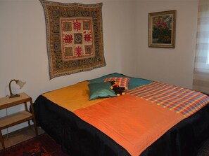 Ein Schlafzimmer mit einem Bett, einer großen Wandteppich, einem gerahmten Bild und einem Schreibtisch mit einer Lampe.
