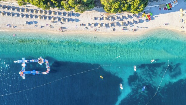 Vue aérienne d’une plage aux eaux turquoise et limpides, avec une jetée et plusieurs bateaux.