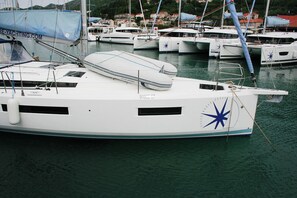 Eine weiße Yacht liegt im Hafen festgemacht, umgeben von anderen Booten, mit einem Stern-Symbol an der Seite und einer blauen Plane am Mast.