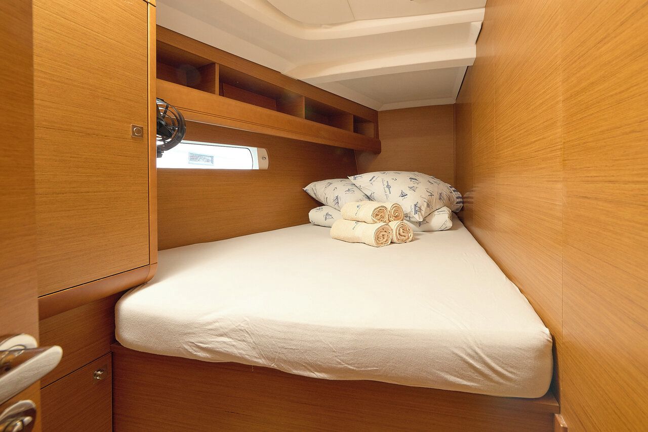A compact, wooden-furnished cabin with a single bed, a small shelf, and a window.