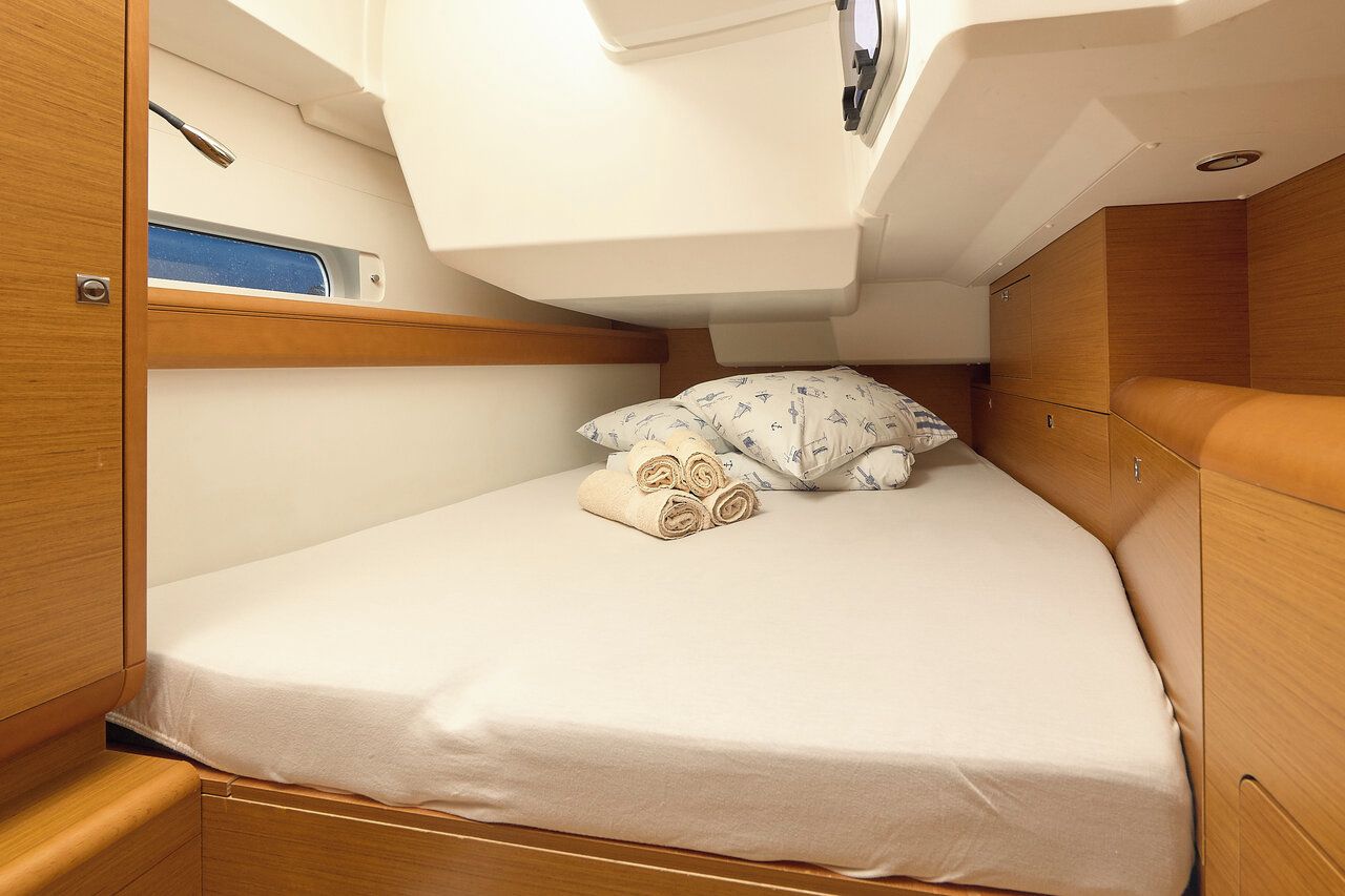 Una cabina compatta e luminosa, con un letto singolo, rivestimenti in legno e una piccola finestra.