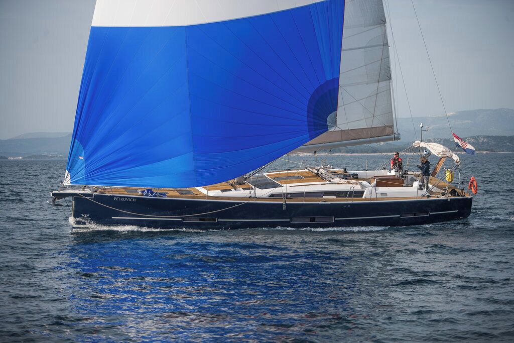 A sailboat with a large blue sail, a cabin, and a deck with people on board.