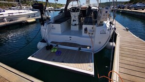 Eine Segelyacht liegt in einer Marina ab, mit überdachter Deckfläche, Steuerrad und kleiner Sitzecke.