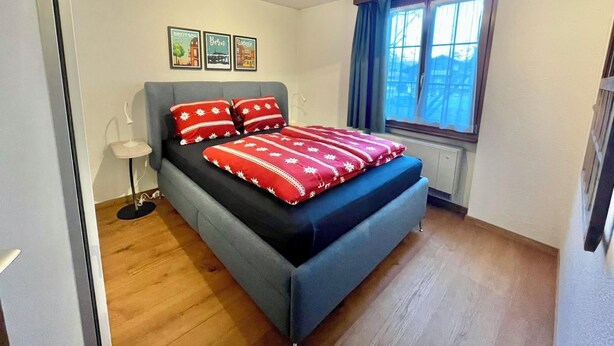 Un dormitorio con cama, lámpara de pie, ventana con cortinas y tres cuadros en la pared.
