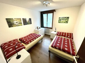 Een kleine, nette kamer met twee enkele bedden, een bureau, een stoel en een raam met gordijnen.
