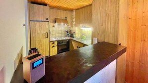 Una cocina compacta con armarios de madera, horno empotrado y un reloj digital.
