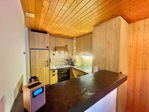 Eine kleine Küche mit Holzausstattung, einem eingebauten Ofen und einer digitalen Uhr.