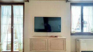 Una sala de estar con un televisor de pantalla plana montado en la pared, un mueble de madera debajo y una puerta corrediza de vidrio a la izquierda.